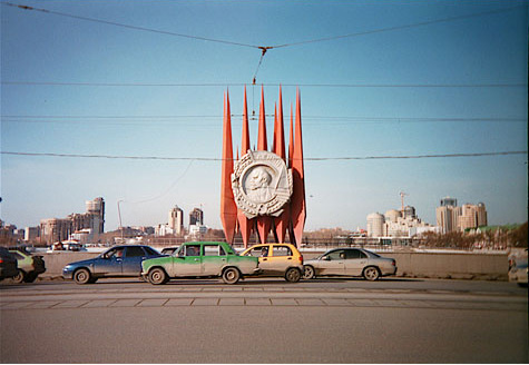 Cars driving the same direction on a large road.  Centered in the background is a large monument.  In the far distance in a city. 