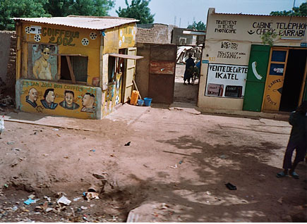 Two makeshift houses decorated in bright colors.  They are surrounded by dirt with debris in the forefront