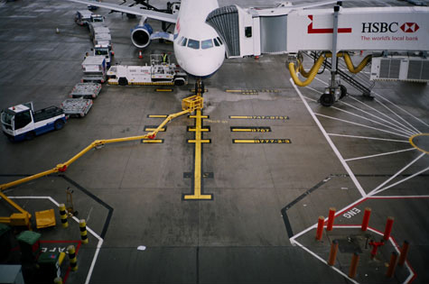 Photograph capturing an airplane on the tarmac and with baggage vehicles and a boarding bridge.  The airplane is centered on a yellow line.