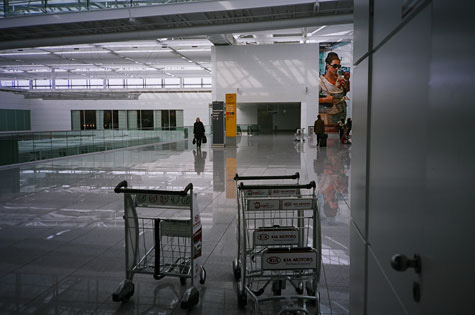 Baggage area of an airport.  The area is empty except for three baggage carts in the forefront and one person in the distance