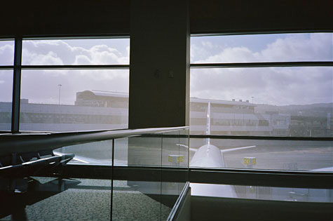 Interior of airport looking out onto the tarmac.  You can see an airplane through the window and also reflected in the interior glass
