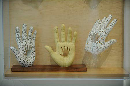 Series of three sculptures.  Two white hands and one yellow hand.  They all have the image of a smaller hand imbedded in the palm of their hands 