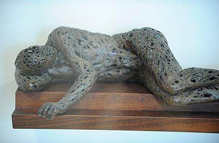 Sculpture of a man laying on his side, on a wooden platform 
