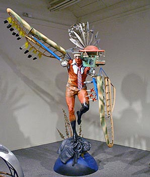 Sculpture of a man with wings standing on one foot, balancing many objects