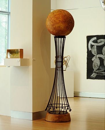 Orange orb on sitting on top of tall black metal sculpture 