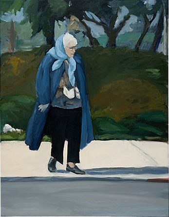 Elderly woman wearing a blue coat and light blue scarf standing on a sidewalk.   